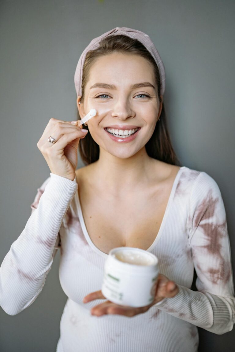 Happy woman applying skincare cream indoors, showcasing a healthy beauty routine.